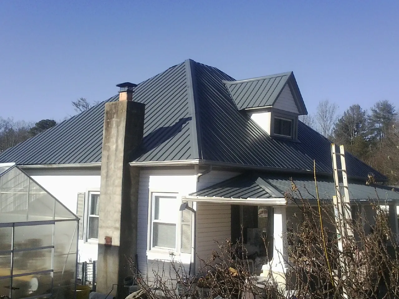Dark blue standing seam metal roof on a white farmhouse with dormer — Slate & Tile Roof Repair by Roofing Brothers in Galena