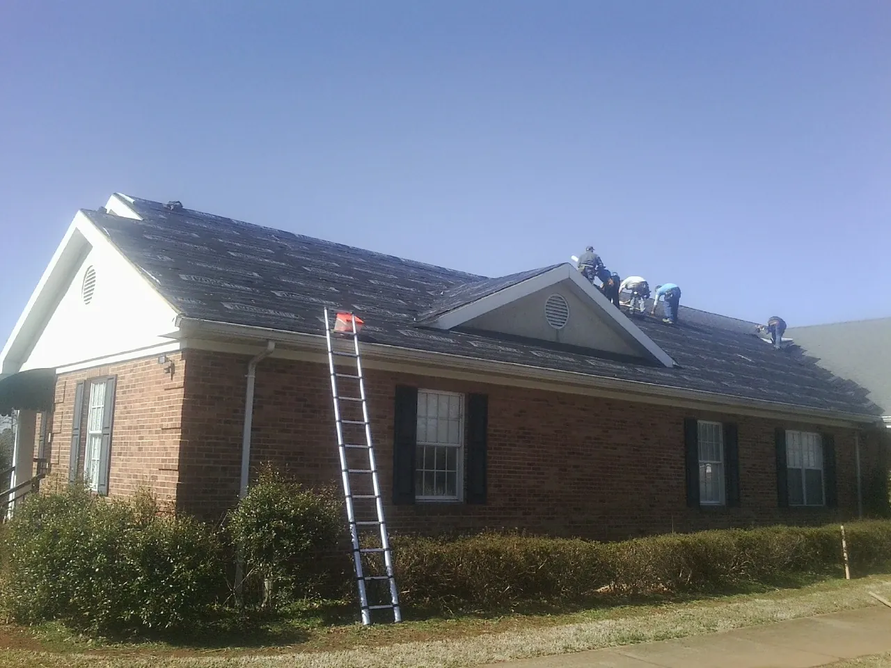 Crew tearing shingles off a brick ranch roof with a ladder set — Metal Roof Repair work by our crew in Galena