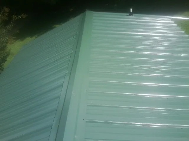 New green metal panels meeting at the ridge of a roof — Flat Roof Repair work by our crew in Galena
