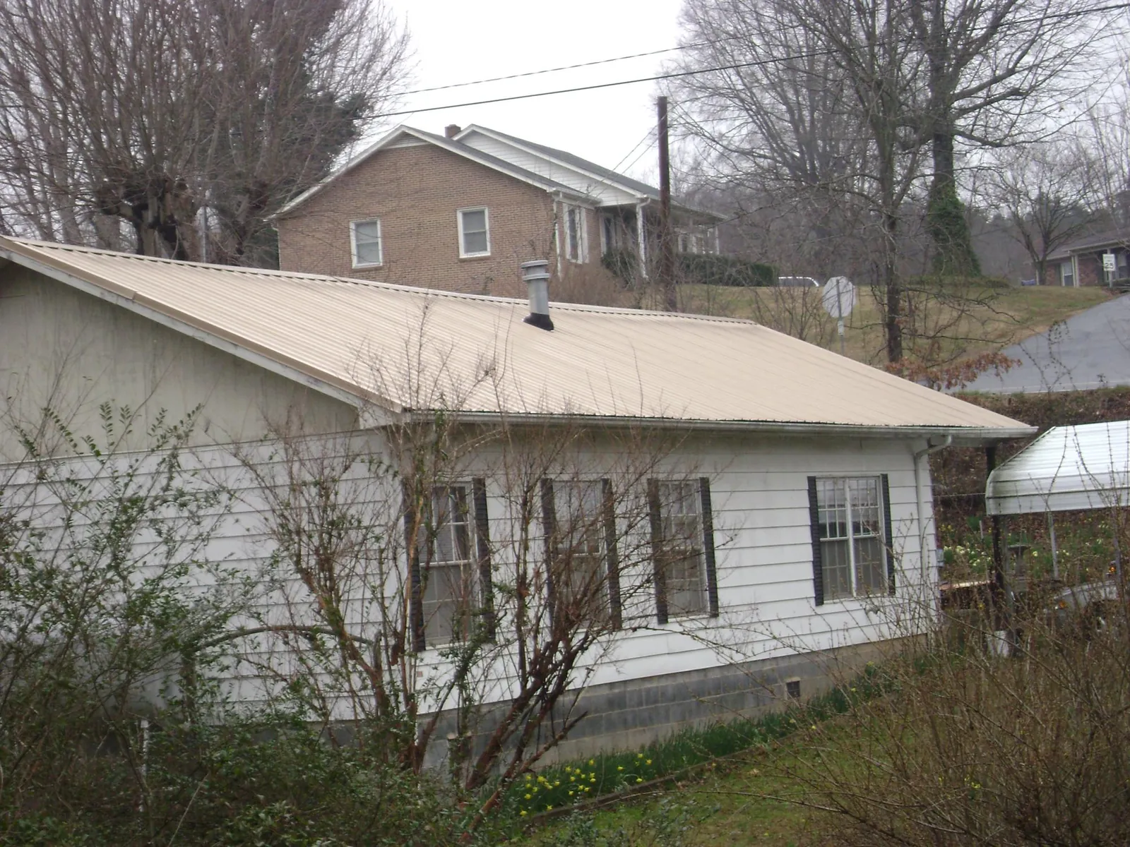 Tan metal roof on a white sided house set into a hillside — Commercial Roofing by Roofing Brothers in Galena