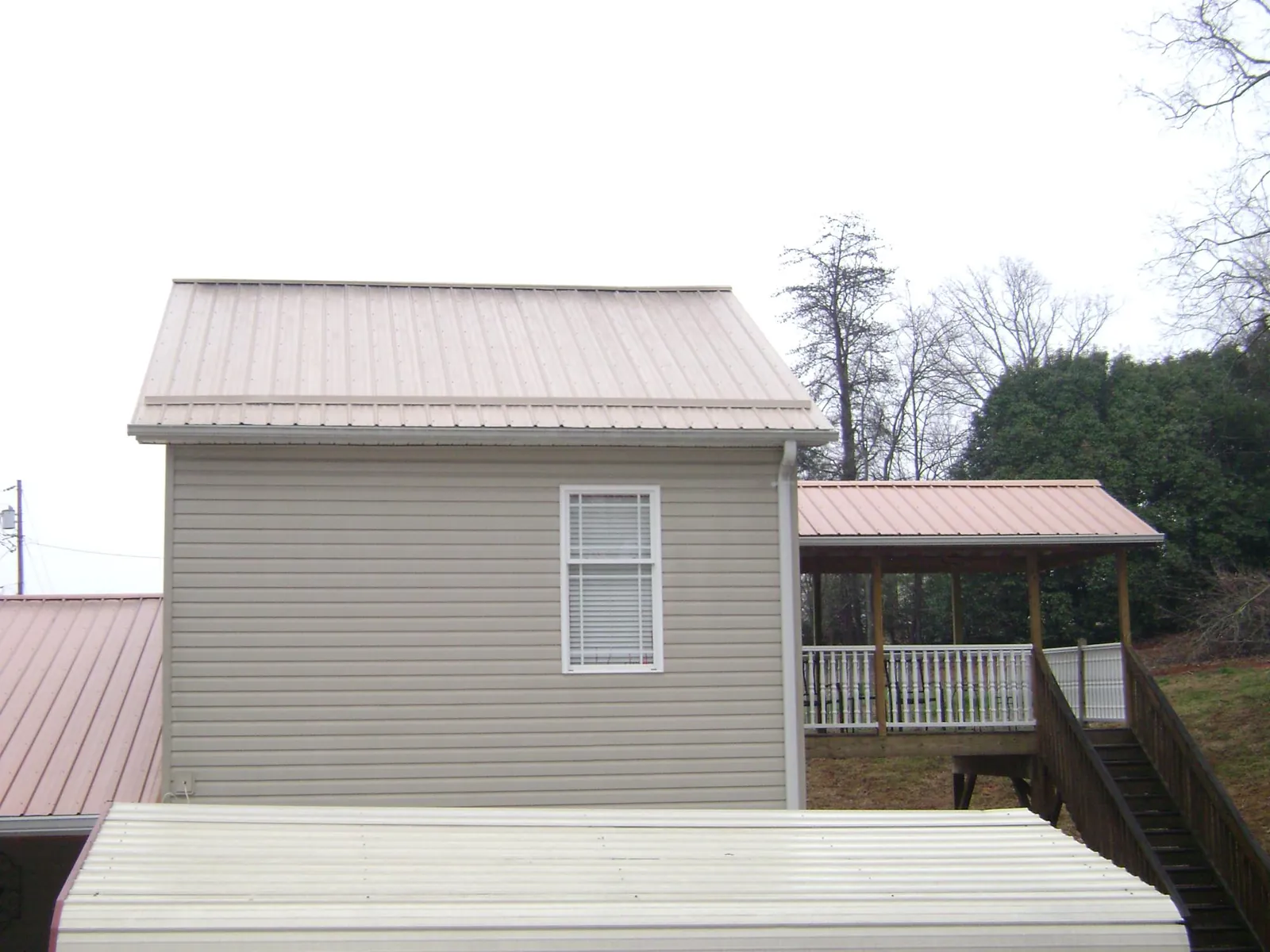 Tan metal roofs on a two story addition and attached porch, from a Roof Replacement job in Galena